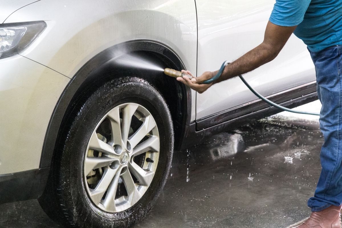 Worker spraying water onto car to wash at garage